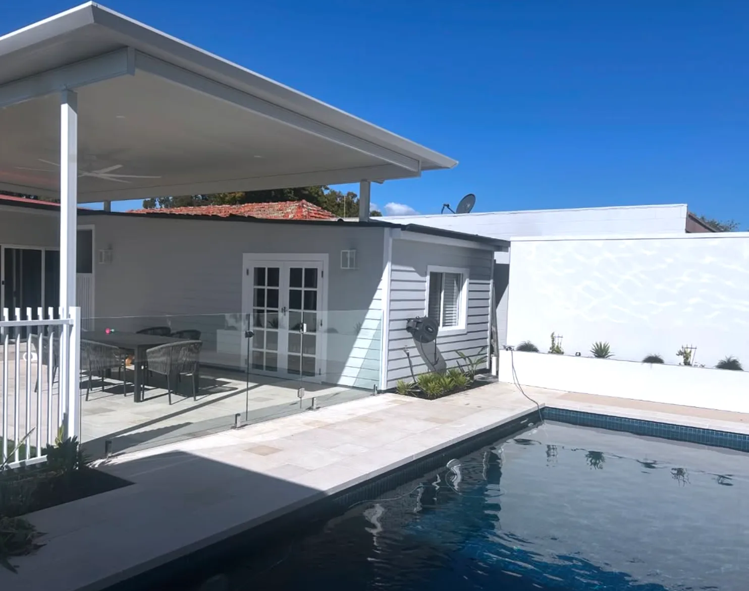Pool house exterior repainted white beside a swimming pool