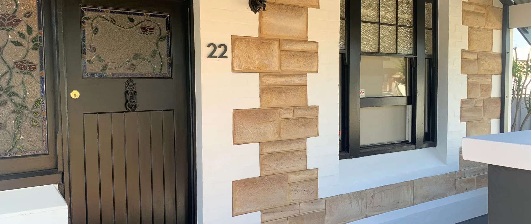 Sandstone house facade with house number 22 beside a freshly painted charcoal front door