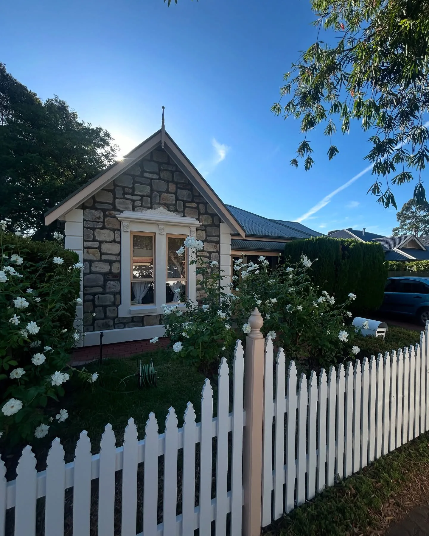 Stone cottage behind a freshly painted white picket fence with white window trims